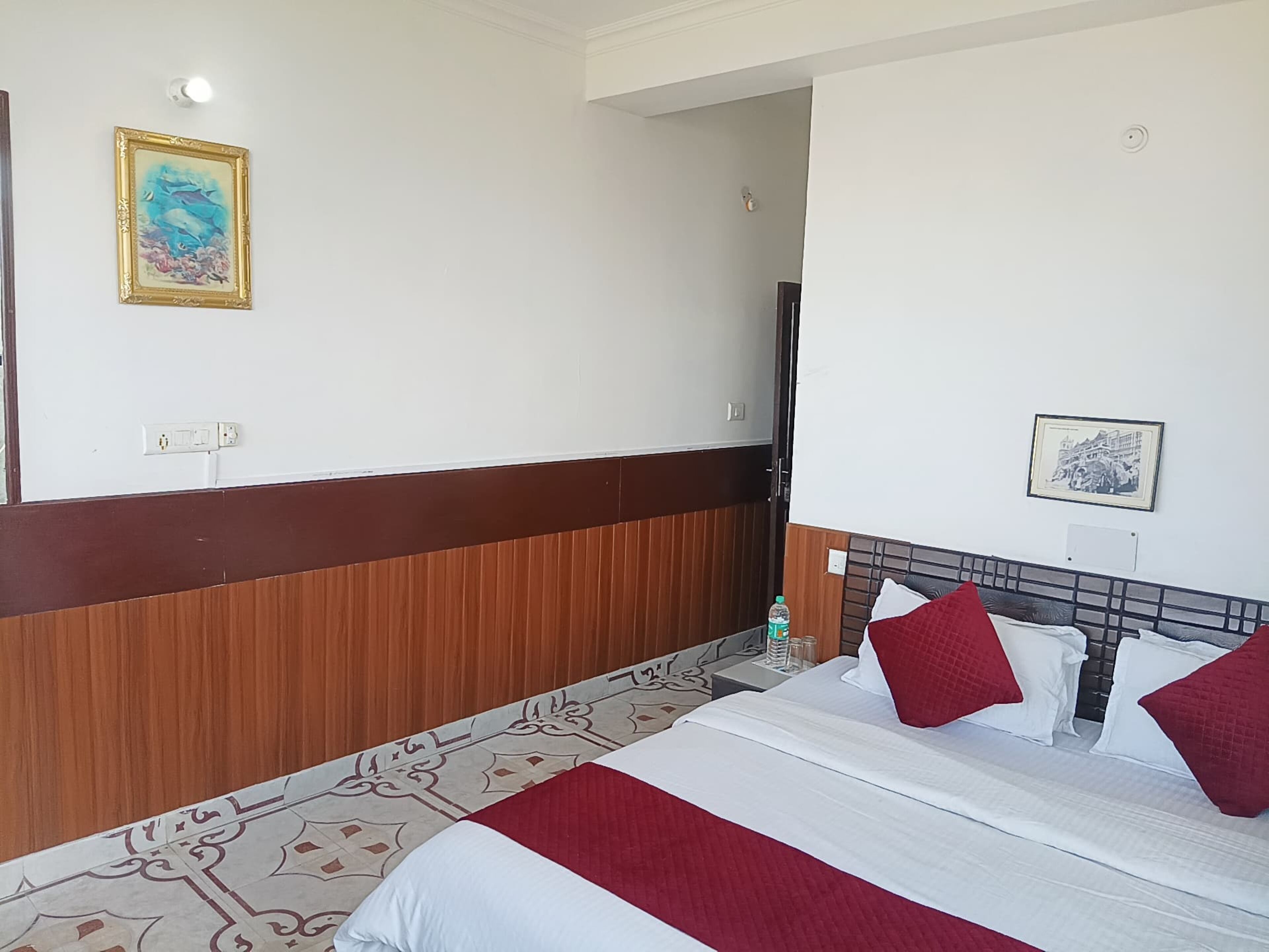 Habitació d'hotel amb llit, capçalera de fusta, quadre penjat a la paret i sòl de rajola.
