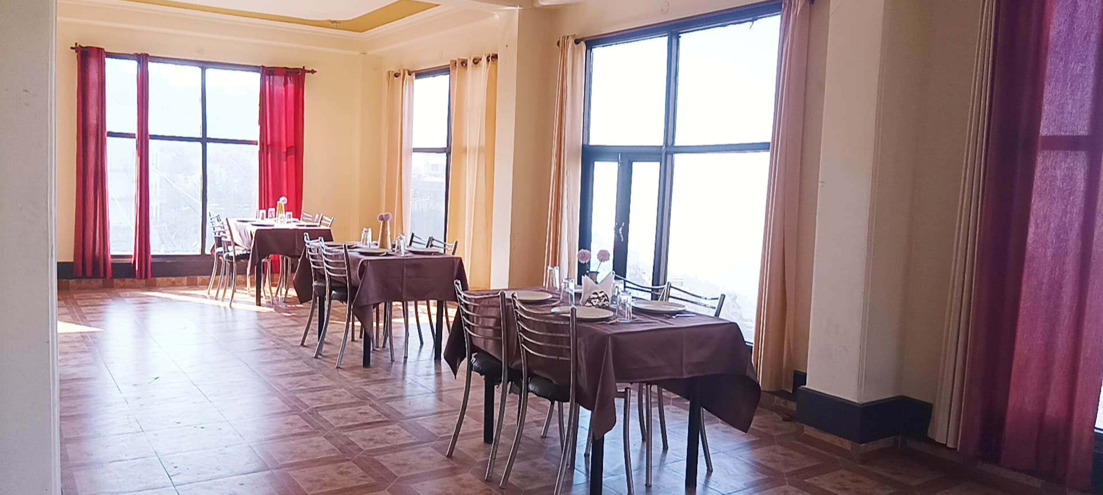 Un espace repas comprenant plusieurs tables et chaises, de grandes fenêtres et des rideaux.