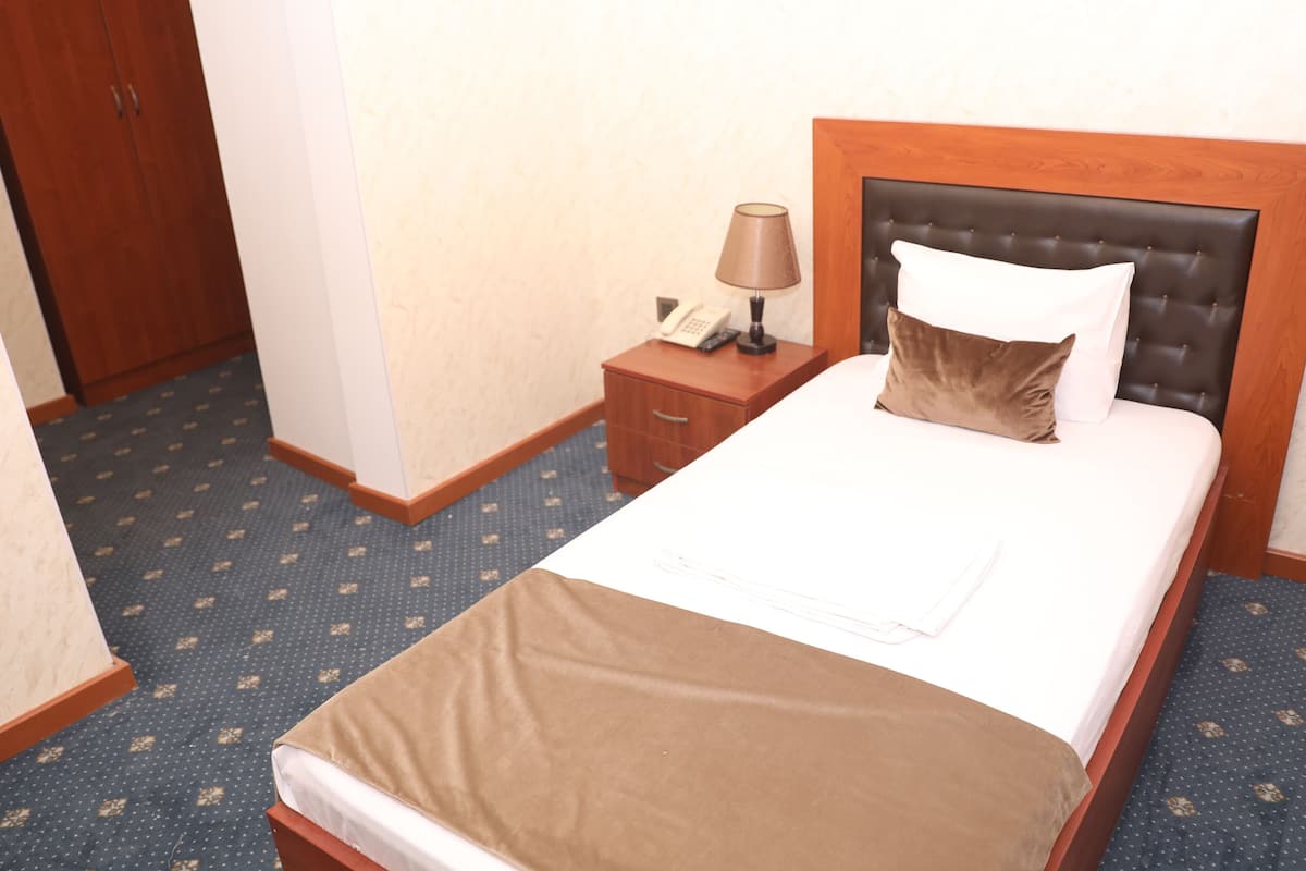 A neatly made bed with a brown blanket, a wooden nightstand with a lamp, and a telephone.
