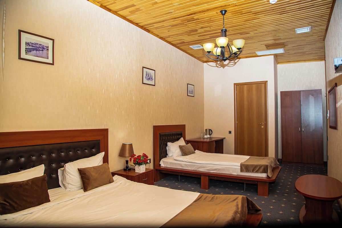A hotel room with two beds, wooden headboards, a chandelier, and a small round table.