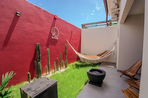 Pared roja con un logotipo, una hamaca, cactus y una maceta negra.