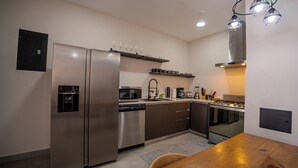 A modern kitchen with stainless steel appliances, a built-in oven, and a microwave. There is a sink with a faucet, a coffee maker, and a toaster. The kitchen has a wooden dining table and chairs.