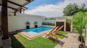 Una piscina con borde de baldosas, rodeada de césped y plantas en macetas.