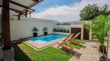Una piscina con borde de baldosas, rodeada de césped y plantas en macetas.