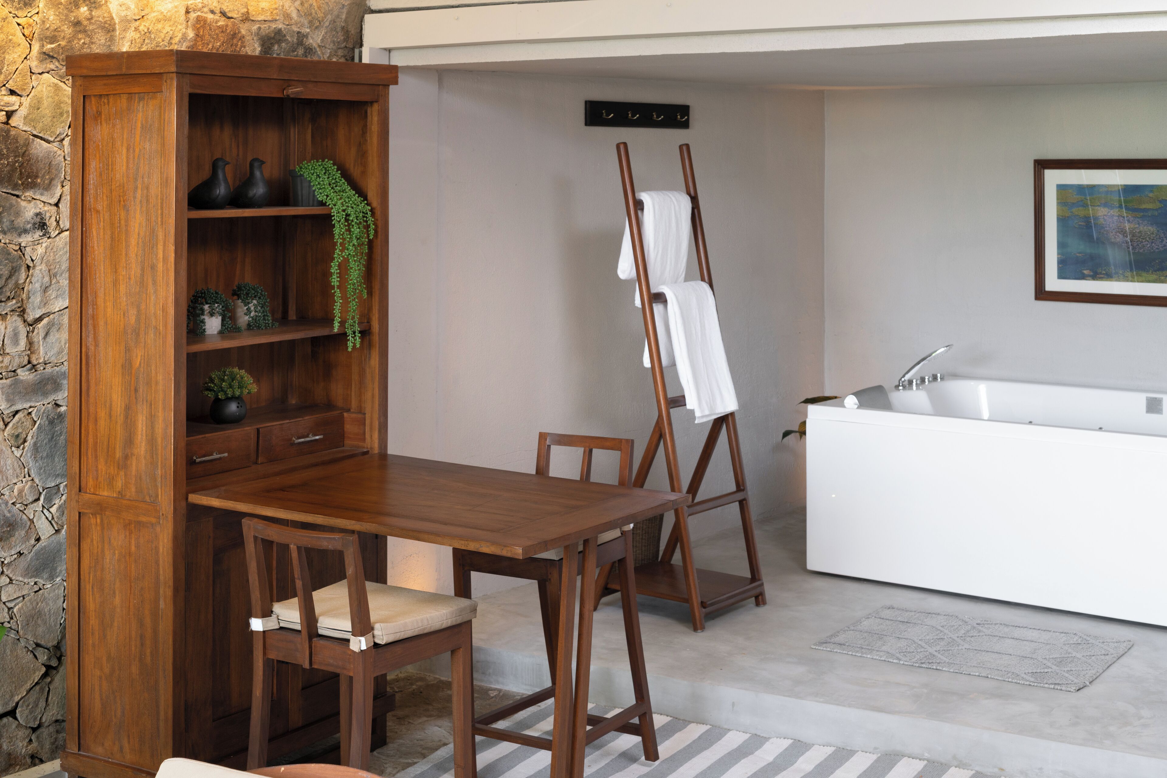 A room with a wooden desk, chairs, a white cabinet, a hanging plant, and a towel rack.