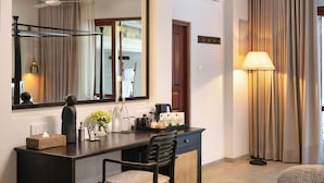 Habitación de hotel con un escritorio de madera oscura, una silla, un espejo grande, una lámpara y vistas al exterior a través de cortinas.