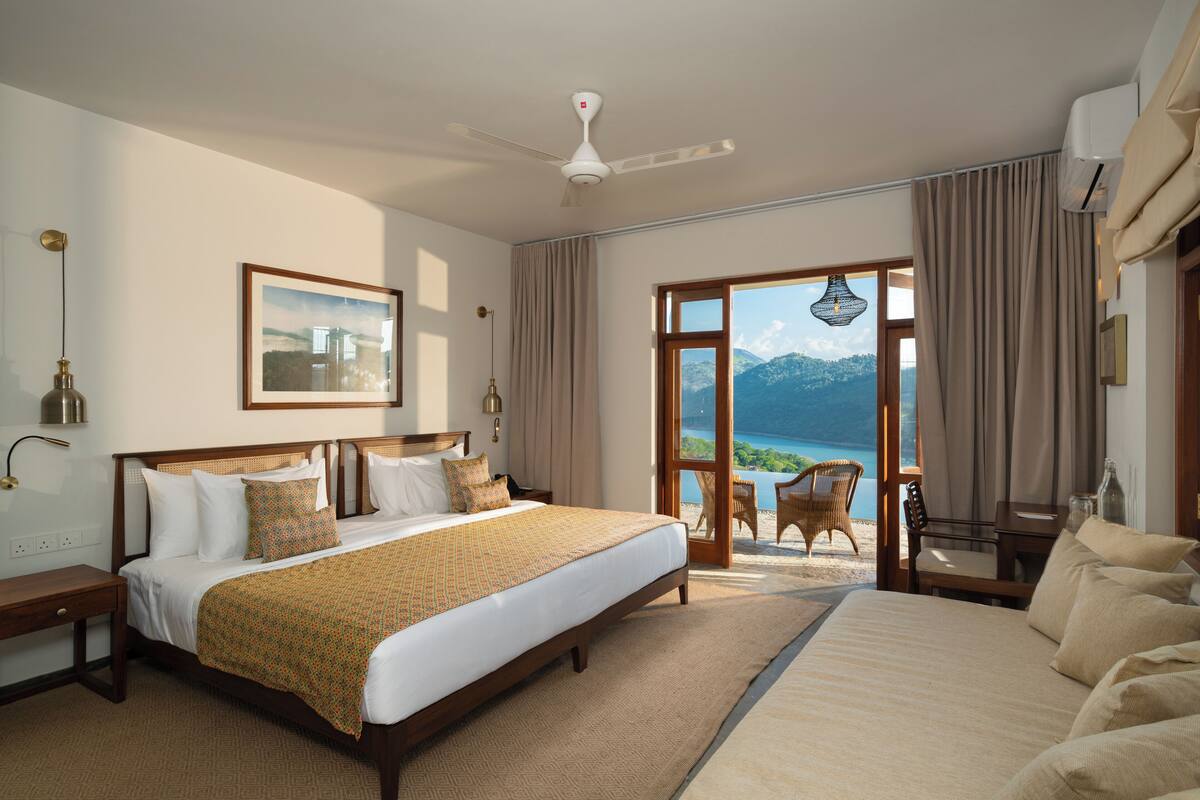 A spacious bedroom with a large bed, a ceiling fan, and a view of the sea through a sliding glass door.