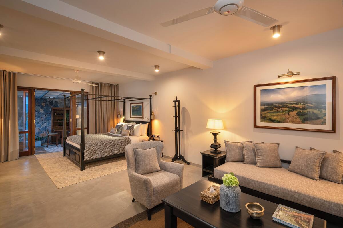 A spacious bedroom with a four-poster bed, a sitting area with a sofa and armchair, and a dining area with a table and chairs.