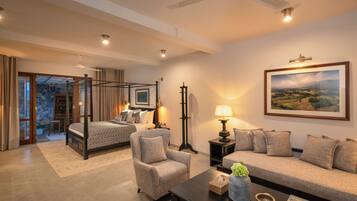 A spacious bedroom with a four-poster bed, a sitting area with a sofa and armchair, and a dining area with a table and chairs.