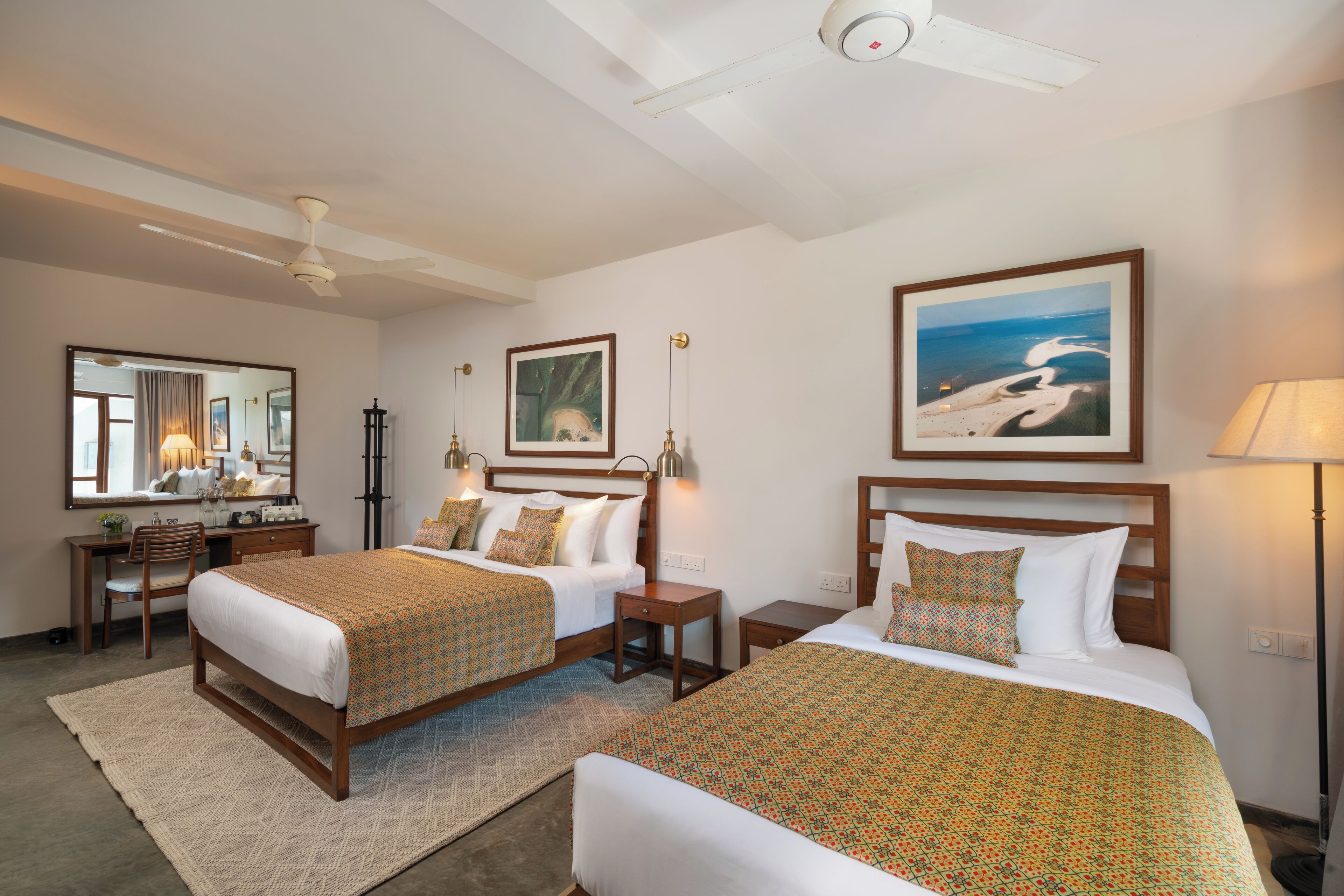 A hotel room with two beds, a desk, a chair, a mirror, and artwork on the walls.
