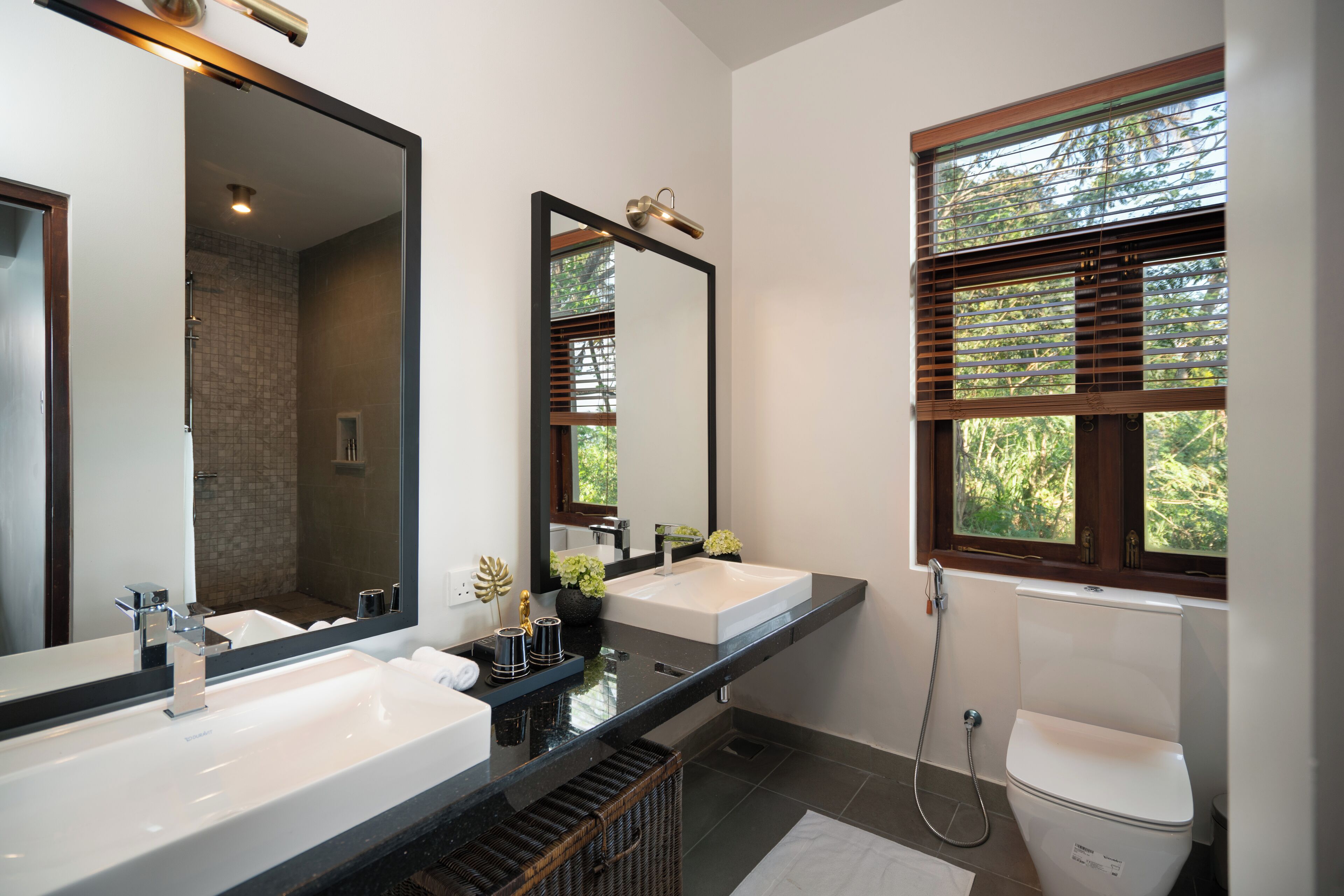 Un baño moderno con dos lavamanos, un espejo grande y una ventana con persianas.