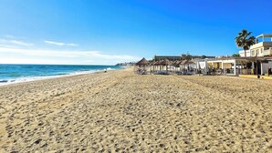 A beach with umbrellas and lounge chairs, a clear sky, and buildings in the background. - Modern 3 bed garden apt next to pool Casa Banderas (La Cala de Mijas)