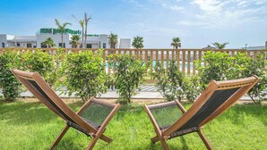 Two wooden lounge chairs with black mesh seats facing a pool area, surrounded by a wooden fence and greenery. - Modern 3 bed garden apt next to pool Casa Banderas (La Cala de Mijas)