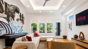 A modern living room with a sofa, ottoman, and a flat-screen TV. - Luxury home with rooftop lounge near Broadway! (Nashville)