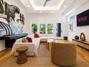 A modern living room with a sofa, ottoman, and a flat-screen TV. - Luxury home with rooftop lounge near Broadway! (Nashville)