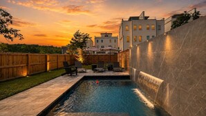 A swimming pool with a waterfall feature, surrounded by a wooden fence and outdoor furniture. - Luxury home with rooftop lounge near Broadway! (Nashville)