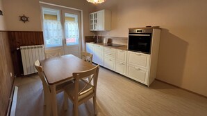 Una cocina compacta con armarios blancos, una mesa de comedor con sillas, un horno empotrado y una lámpara colgante.