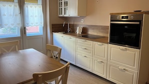 Una cocina compacta con armarios blancos, encimera de madera, horno empotrado y una ventana con cortinas a corazón.
