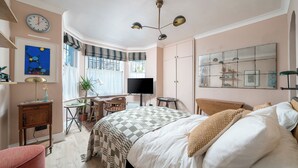 A bedroom with a bed, a desk, a chair, a television, and a large window. - Charming Studio moments from Portobello (London)