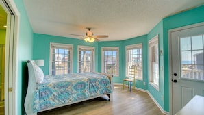 Ein Schlafzimmer mit Bett, Deckenventilator und großen Fenstern.