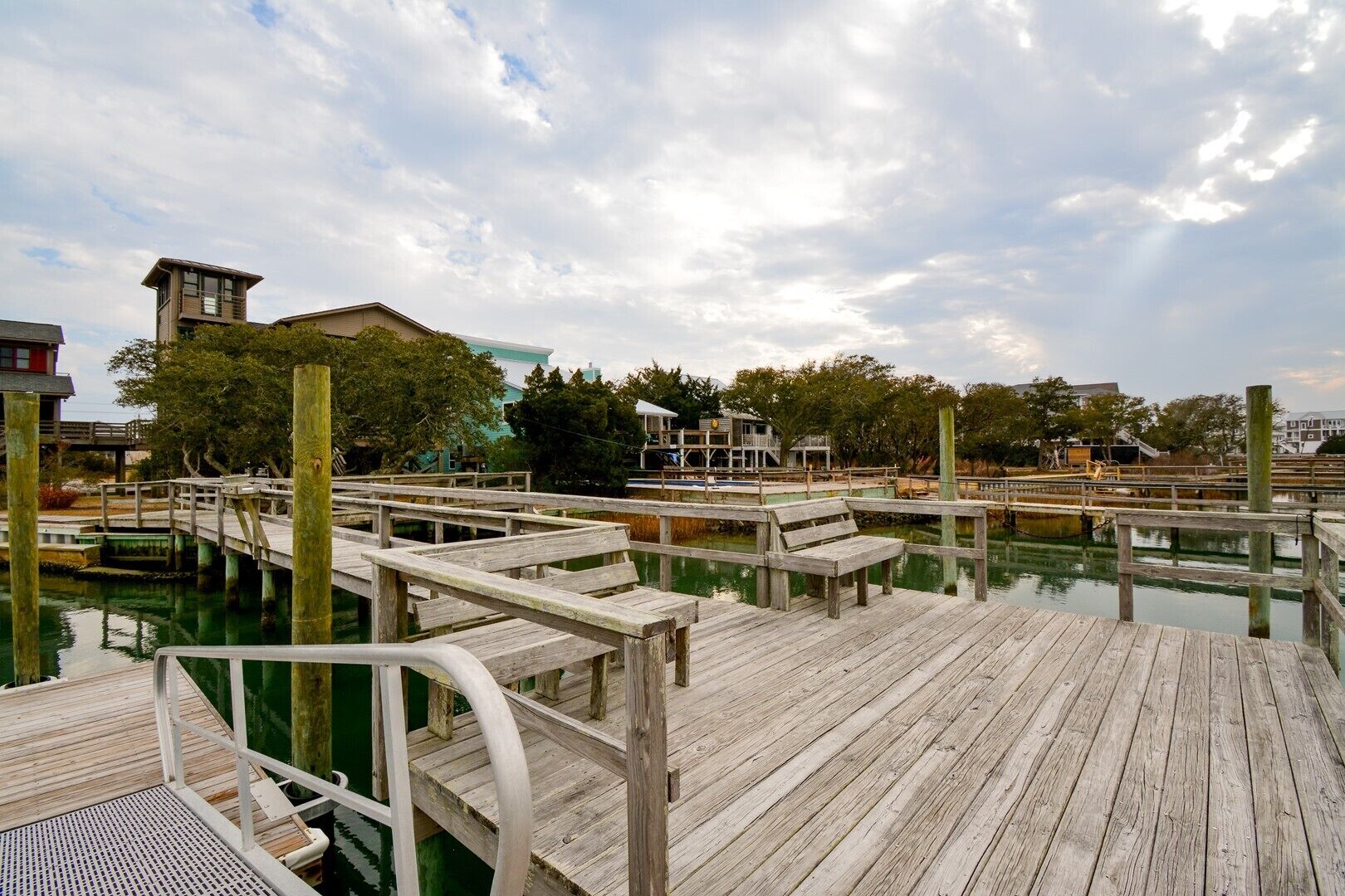 A wooden pier with a metal railing, leading to a dock area with a building in the background.