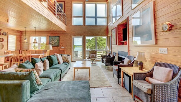 A spacious living room with a high ceiling, wooden walls, and large windows.