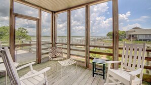 A covered outdoor deck with wooden railings, white chairs, and a small table.