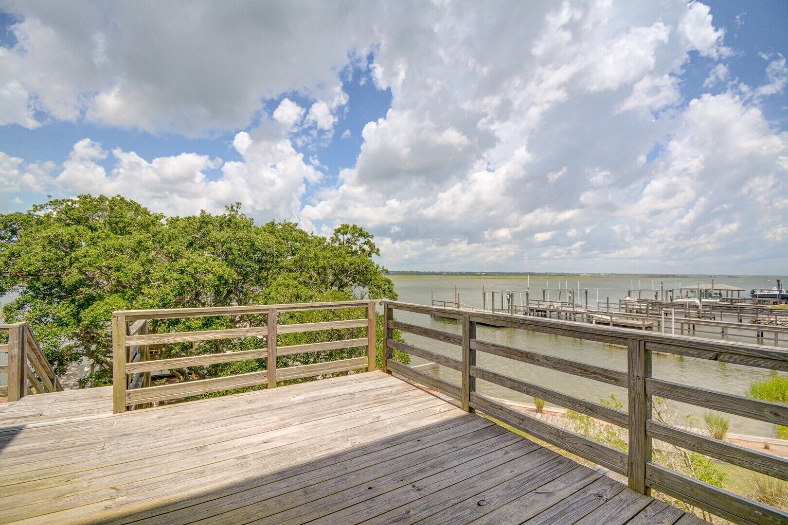 A wooden pier with a railing overlooking a body of water and a dock area.