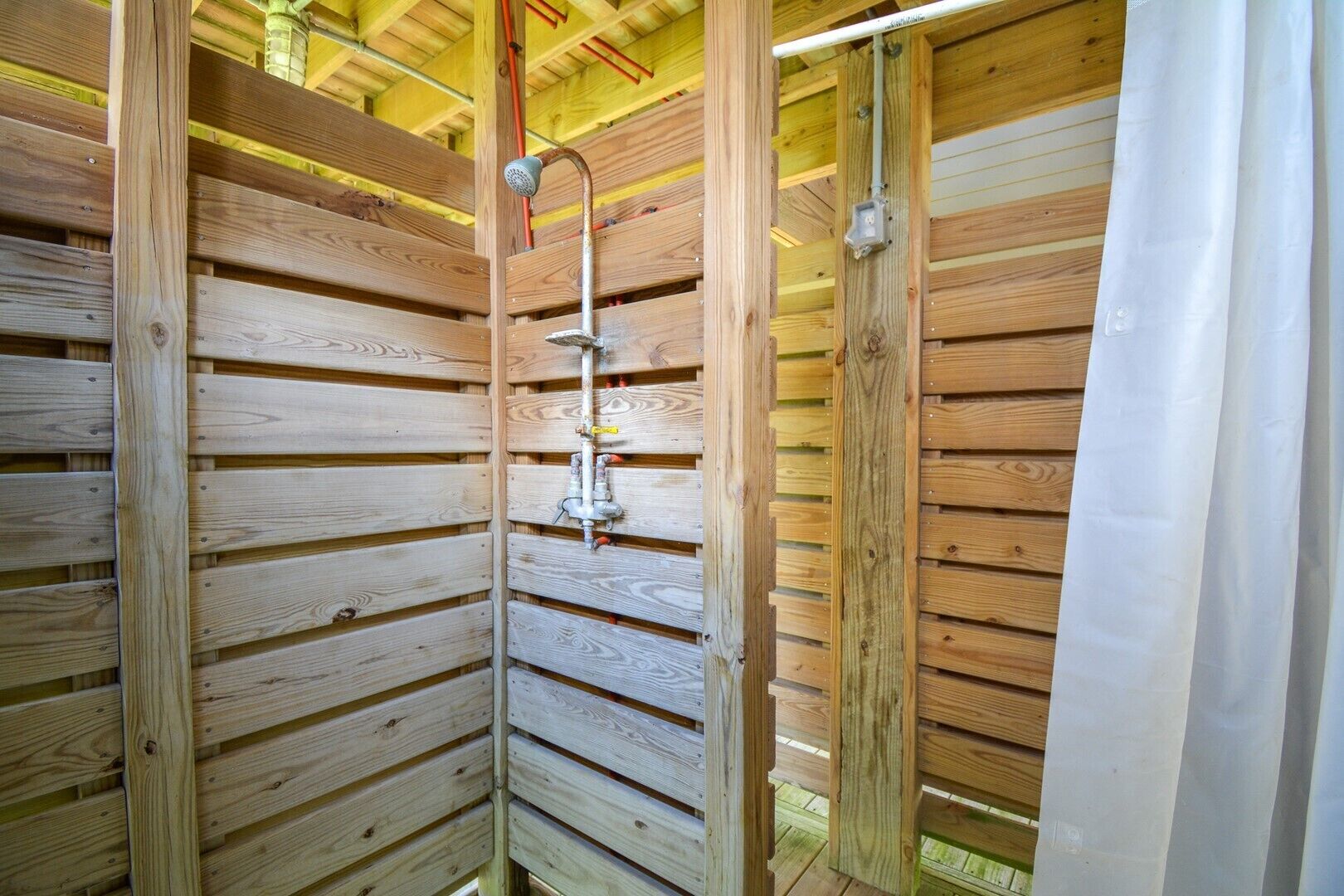 A wooden cabin with a shower area, including a showerhead and pipes.