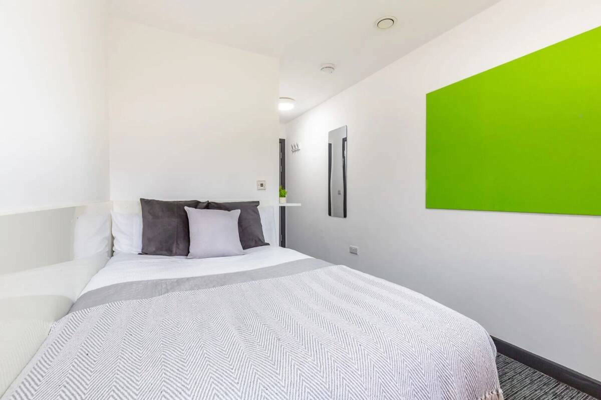 A modern hotel room with a bed, a green accent wall, and a minimalist design.