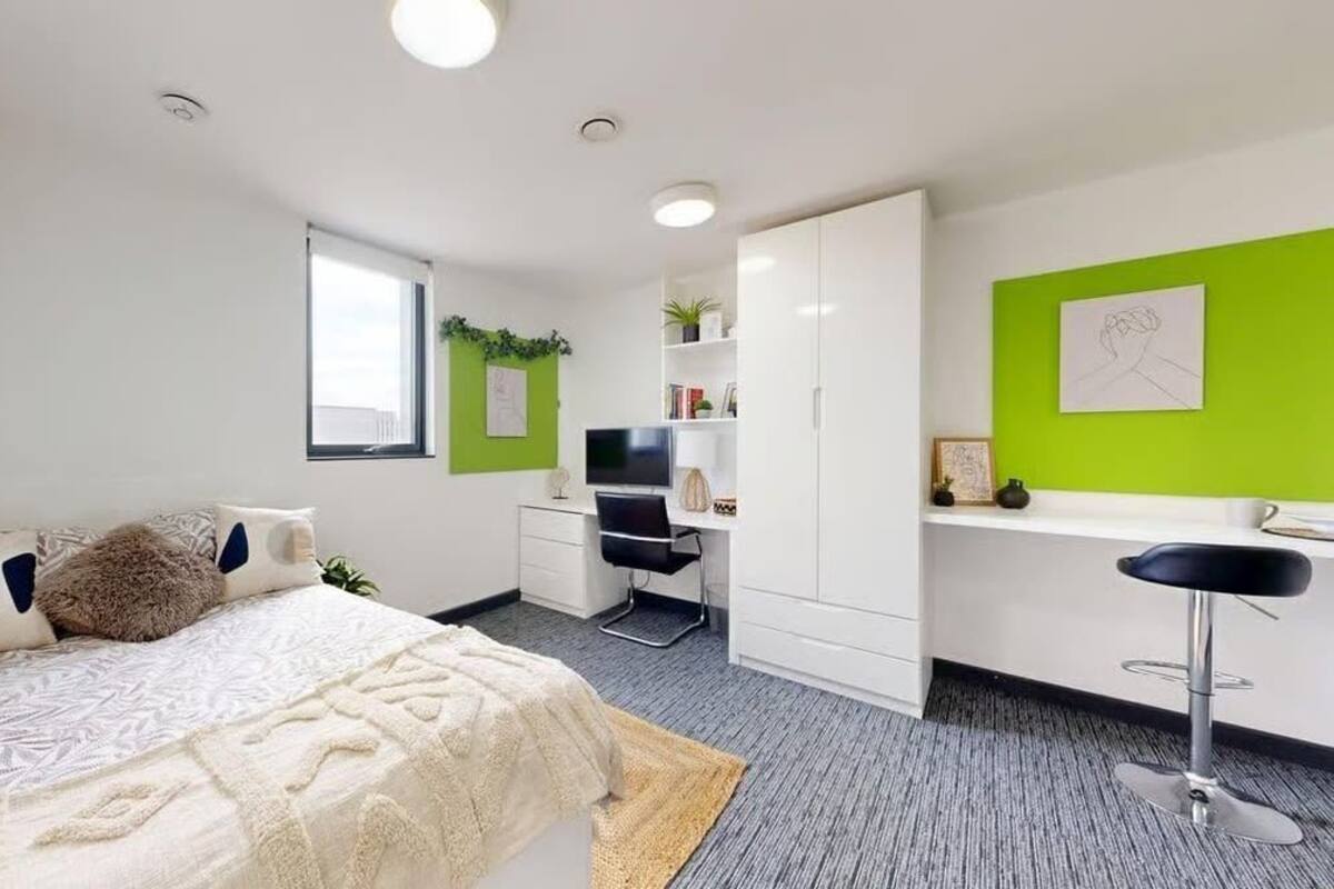 A modern bedroom with a bed, desk, and chair, a small window, and a green accent wall.