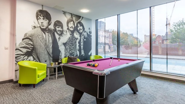 Uma mesa de bilhar com bolas, uma cadeira verde e um mural com uma banda na parede.