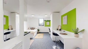 Quarto de hotel moderno com cama, escrivaninha, cadeira, uma planta pequena e janela.