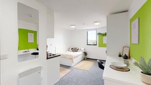 Quarto moderno e bem iluminado com cama, pequeno espaço de cozinha, banheiro e área de jantar.