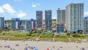 A beachfront hotel with multiple high-rise buildings, a sandy beach, and several umbrellas. - Palms Resort 1406 - Oceanfront! (Myrtle Beach)