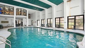 An indoor swimming pool with clear water, surrounded by white walls and large windows. - Palms Resort 1406 - Oceanfront! (Myrtle Beach)