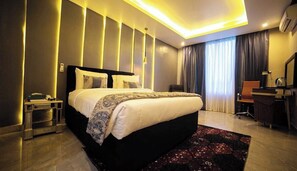 Een moderne hotelkamer met een groot bed, nachtkastjes, een bureau, een stoel en een groot raam met gordijnen.