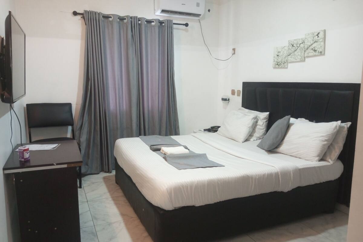 A hotel room with a bed, a desk, a chair, a TV, and a window with curtains.