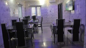 A dining area with marble walls, a TV mounted on the wall, and a window with blinds. - Ted G Hotel (Port Harcourt)