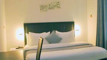 Una habitación de hotel con una cama grande, una mesita de noche, una lámpara y un aire acondicionado.