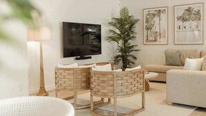 En stue med fjernsyn, to fletstole, en sofa og en plante.