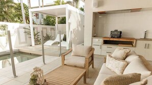 En moderne stue med pool, sofa, sofabord og et køkkenområde med grill.