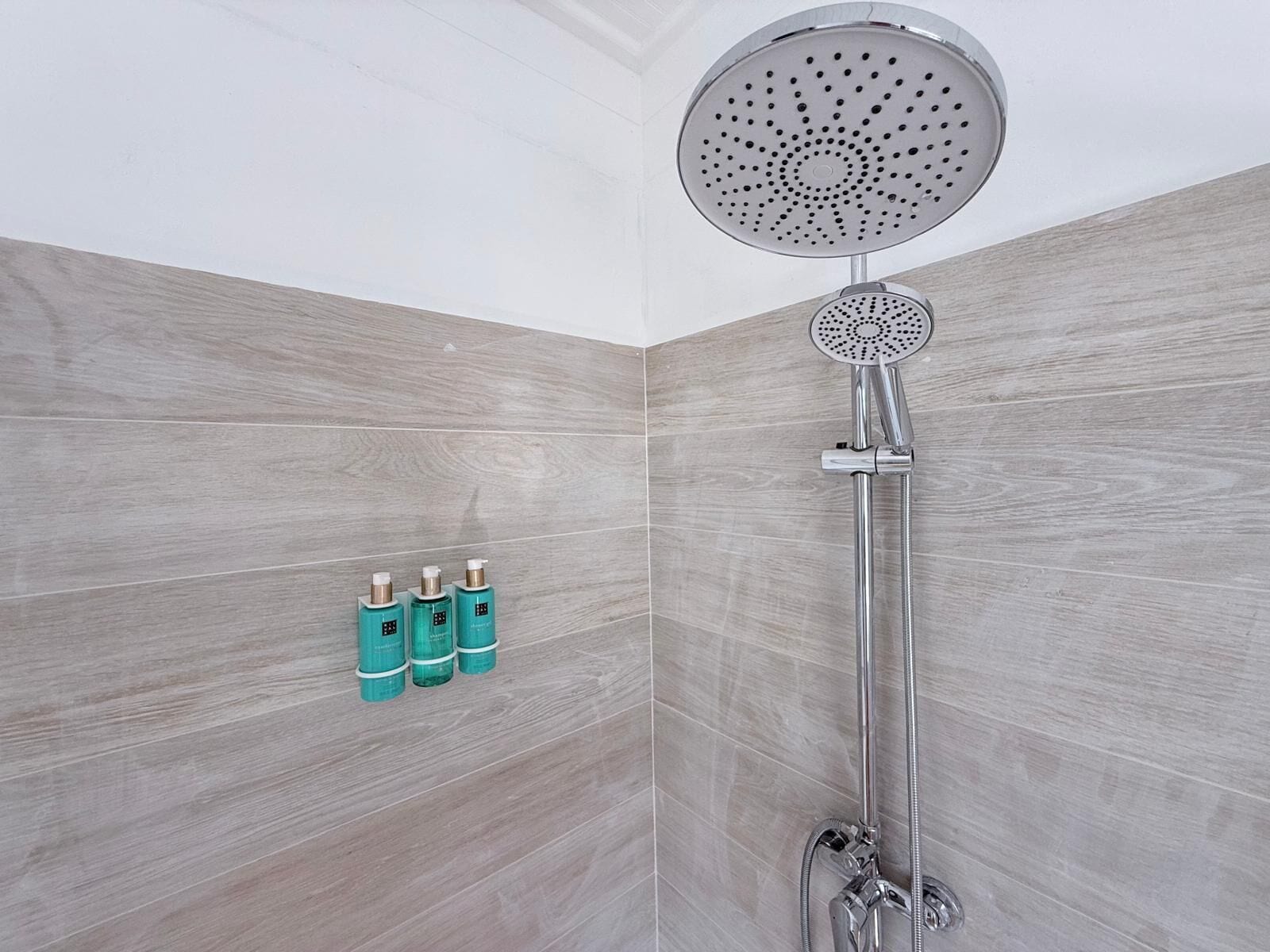 Douche met een ronde douchekop en een handdouche, bevestigd aan een wand met een licht houten afwerking.