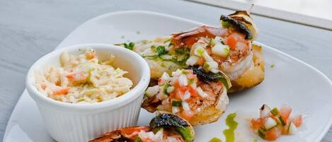 A plate of grilled shrimp with a side of coleslaw and a small bowl of salsa.