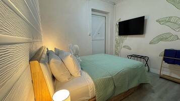 A bedroom with a bed, pillows, a bedside lamp, a TV on the wall, and a towel rack.