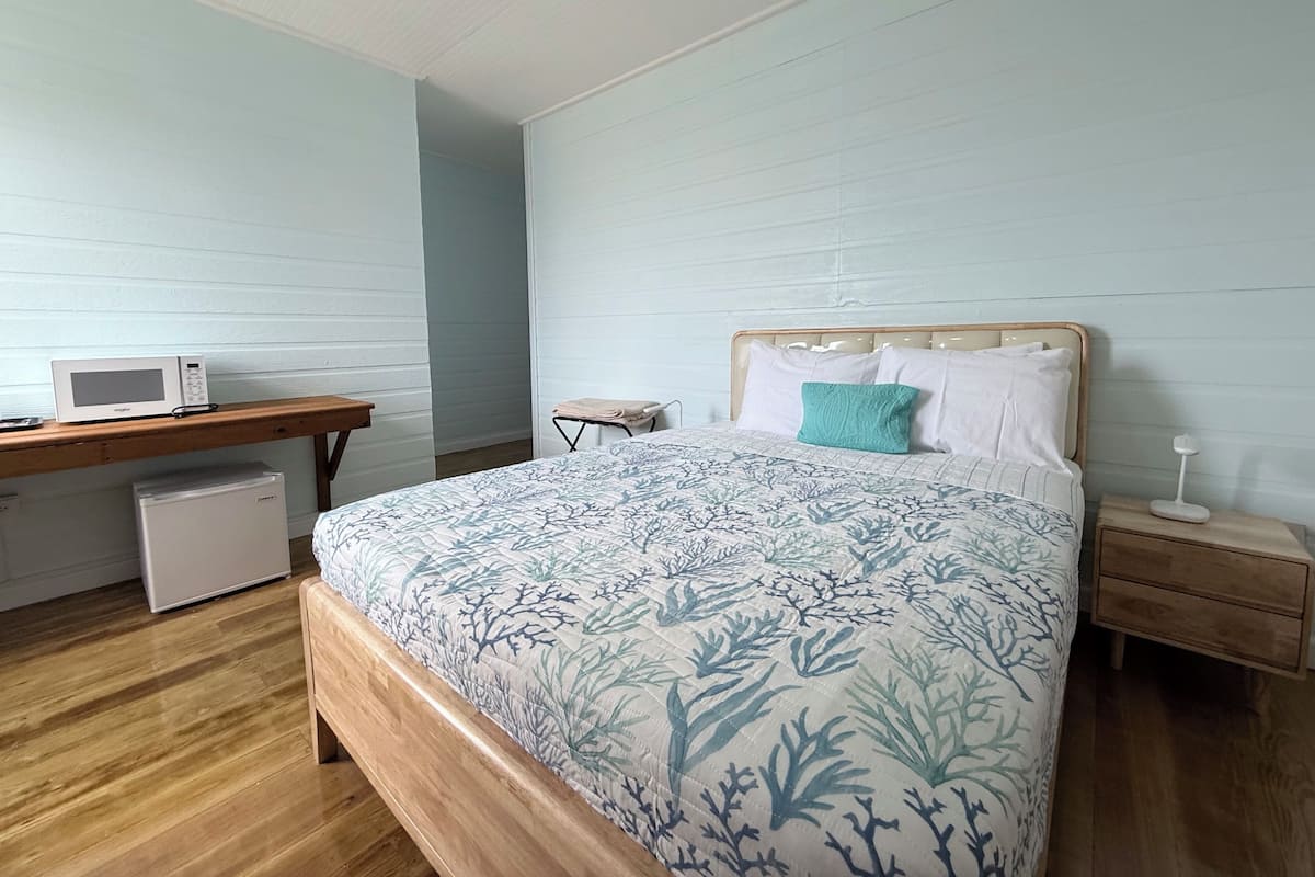 A bedroom with a bed, a desk, a microwave, and a refrigerator.