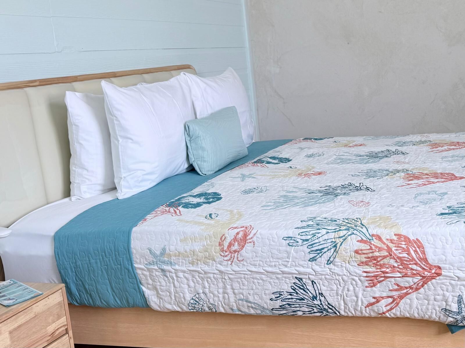 Ein Bett mit floraler Stegdecke, einem Holzkopfende und einer blauen Tagesdecke.