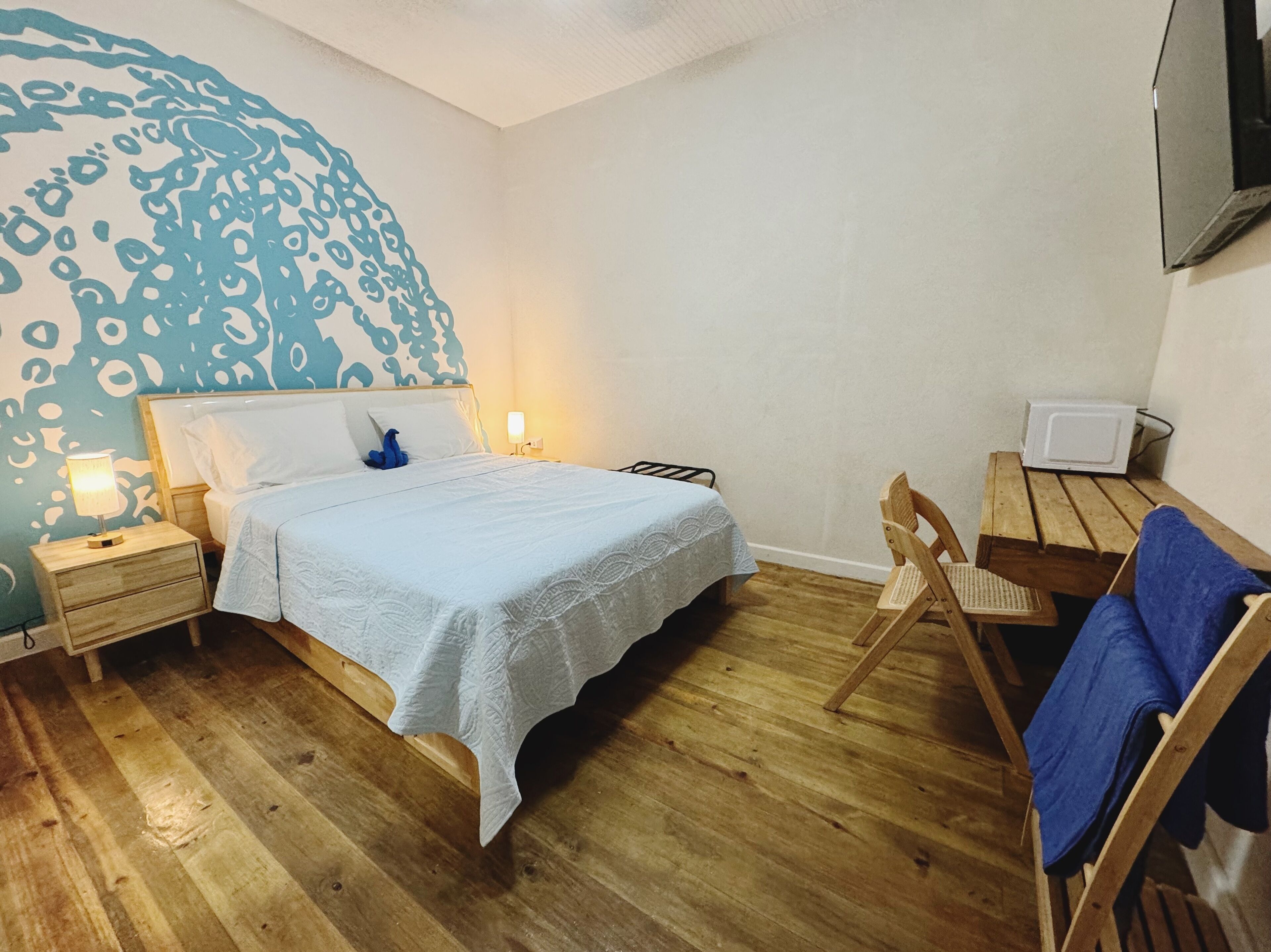 A bedroom with a bed, bedside tables, a chair, a desk, and a TV.