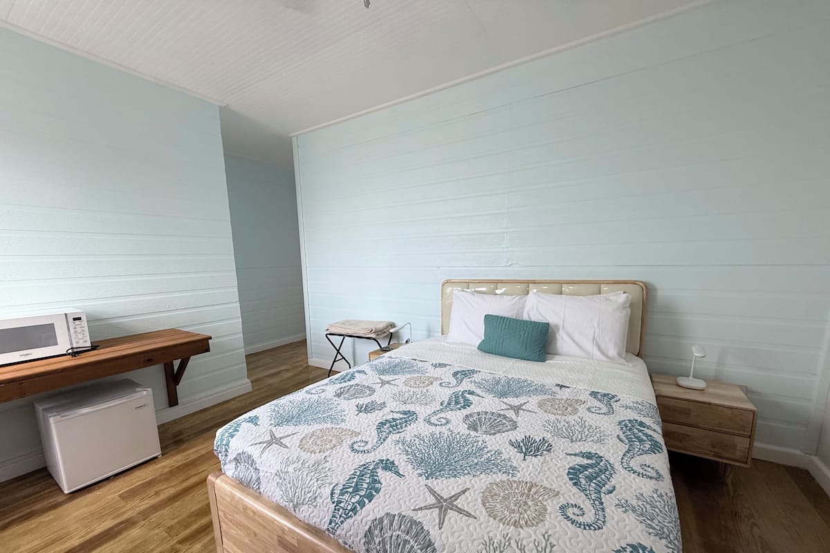 A bedroom with a wooden bed, a nightstand, a bedside table, a microwave, and a small chair.