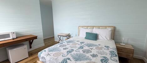Une chambre avec un lit en bois, une table de chevet, une commode, un four à micro-ondes et une petite chaise.